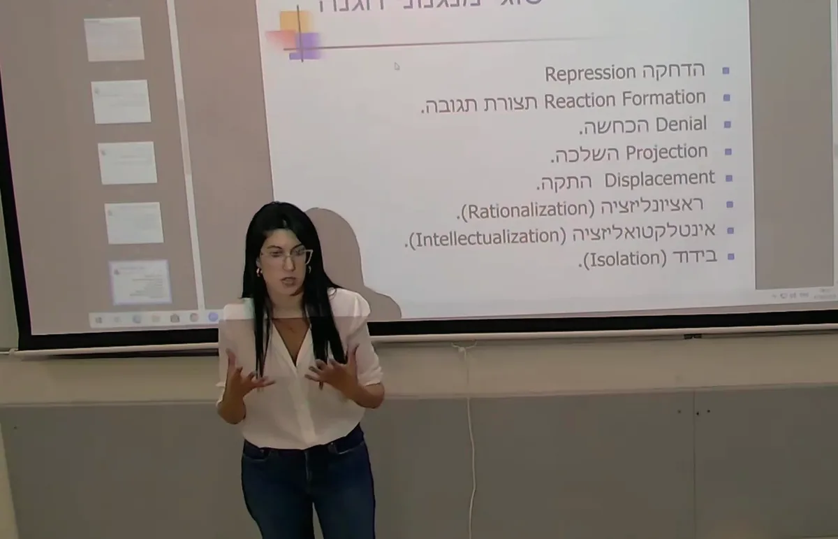ד״ר מאיה שפיגל מרצה מול מסך מצגת אקדמית